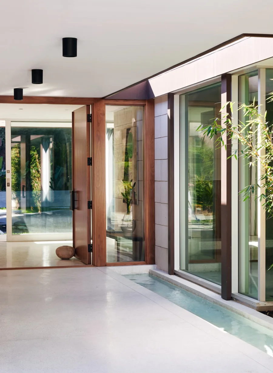 The entry of 1061 Loma Vista, Beverly Hills: a tall pivot door in a glazed wall, stone underfoot.