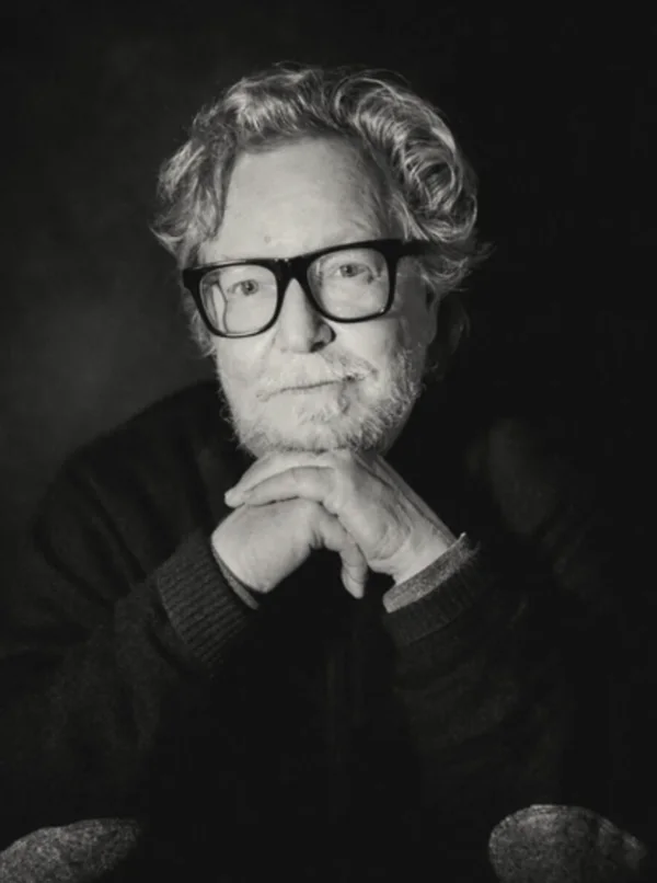 Jacobsen in a black-and-white portrait, hands clasped under the chin, dark-rimmed glasses.