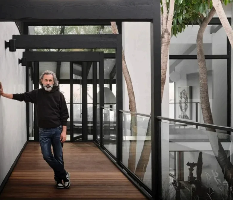 Philippe Naouri on the glazed bridge of a Modernist house, one hand on the wall, trees rising through the courtyard beside him.