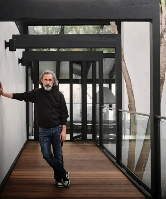 Philippe Naouri on the glazed bridge of a Modernist house, trees rising through the courtyard beside him.