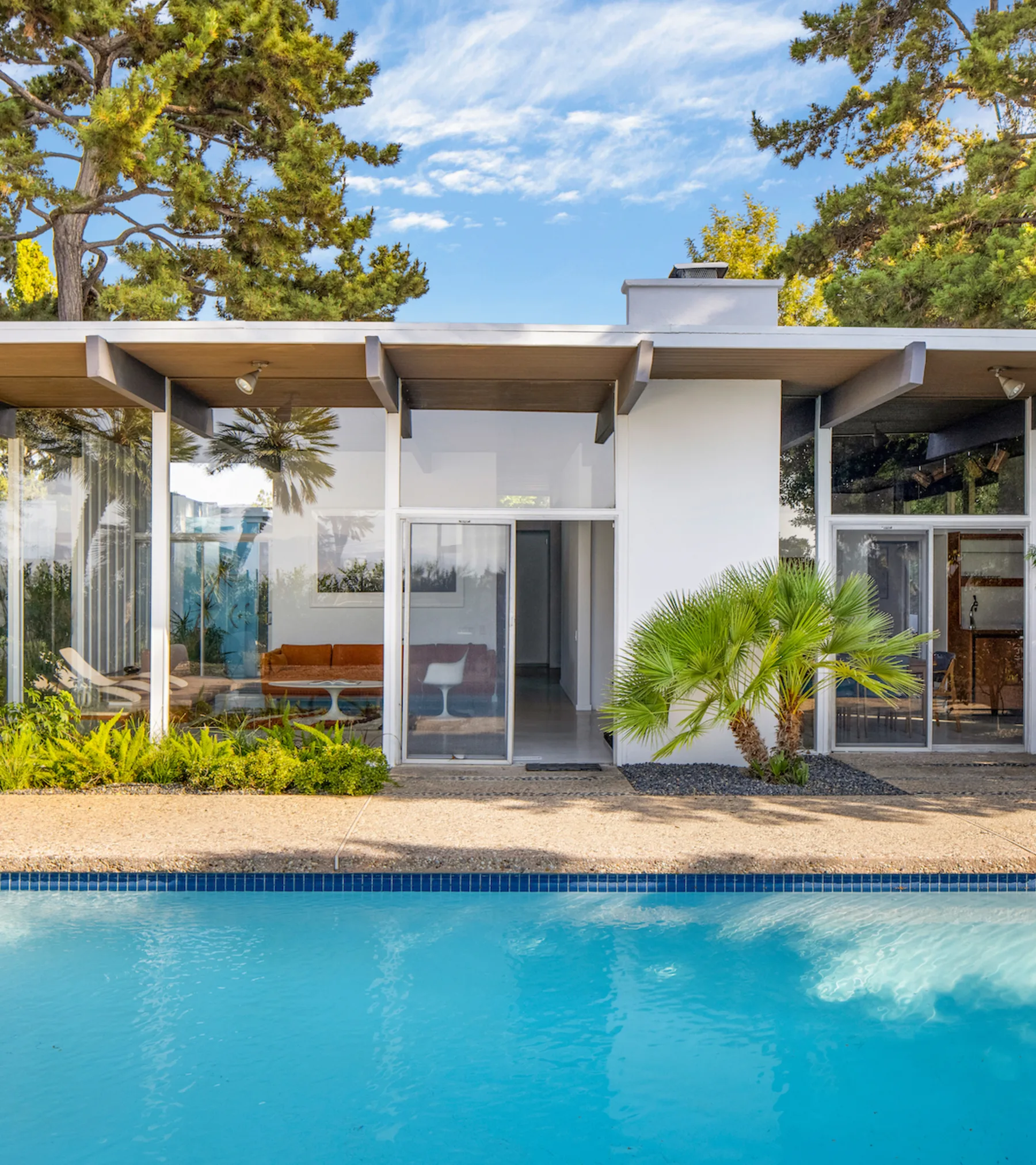 The Calvin House: wide eaves and glass walls over the pool, in afternoon light.