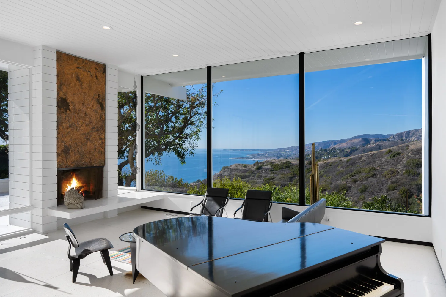 The living room by day: the fireplace, low chairs and the ocean through the glass.