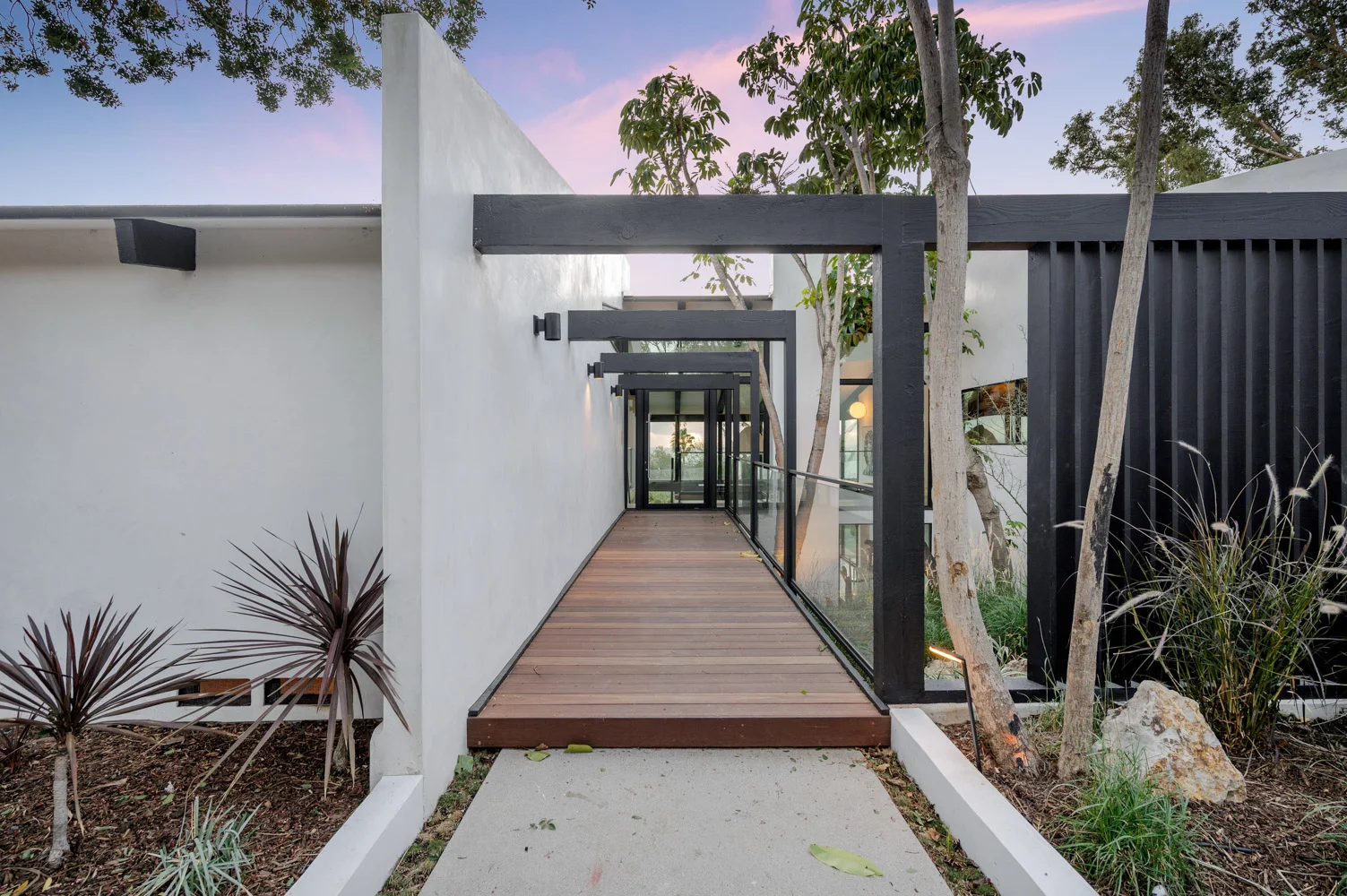 The main entrance: a timber walkway between white walls under a black steel frame.