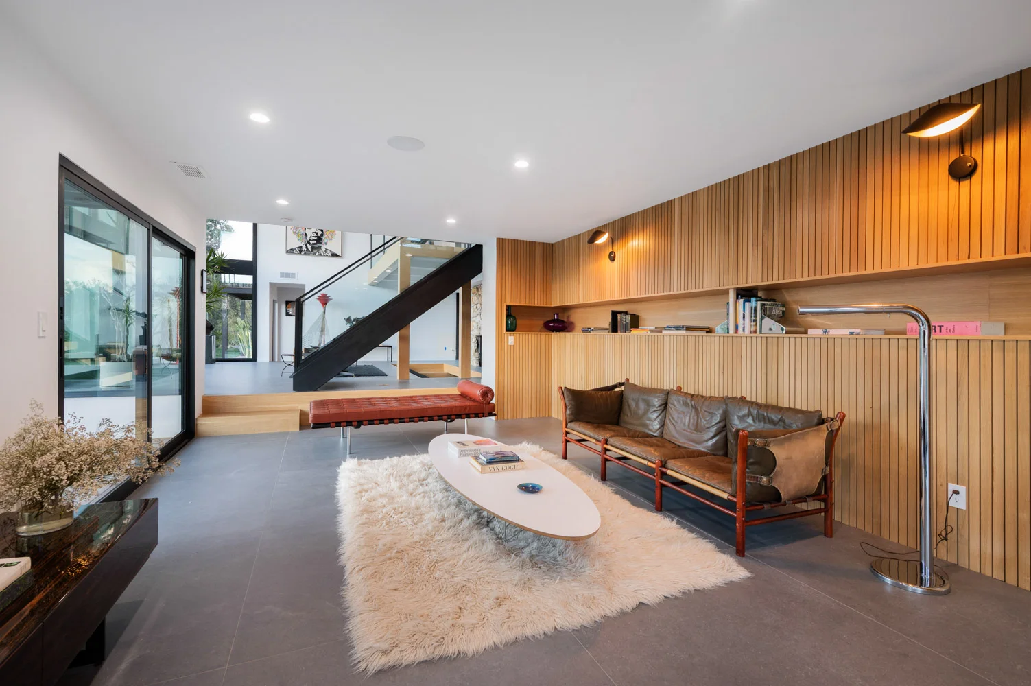 The living room: a slatted wood wall, a long sofa, a fur rug and a surfboard table.
