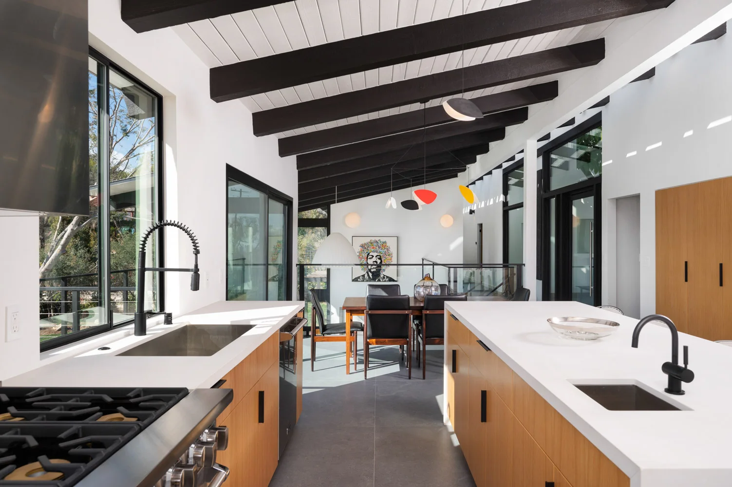 The kitchen and living room under the black beams, ocean light through the glass.