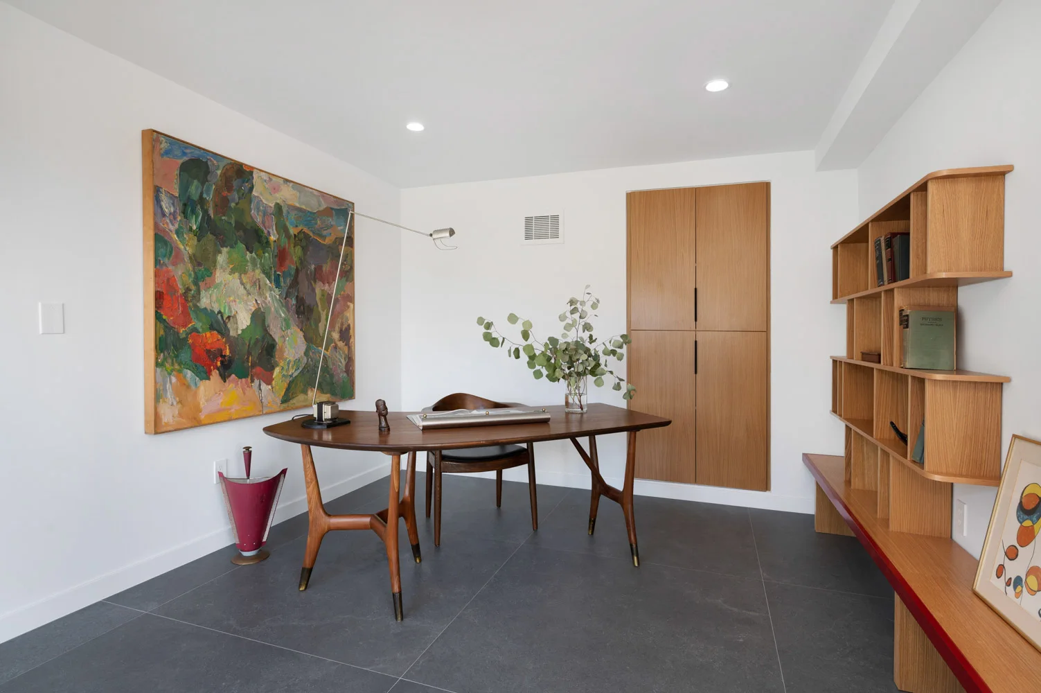 The office: a desk, a painting and a shelf of books.