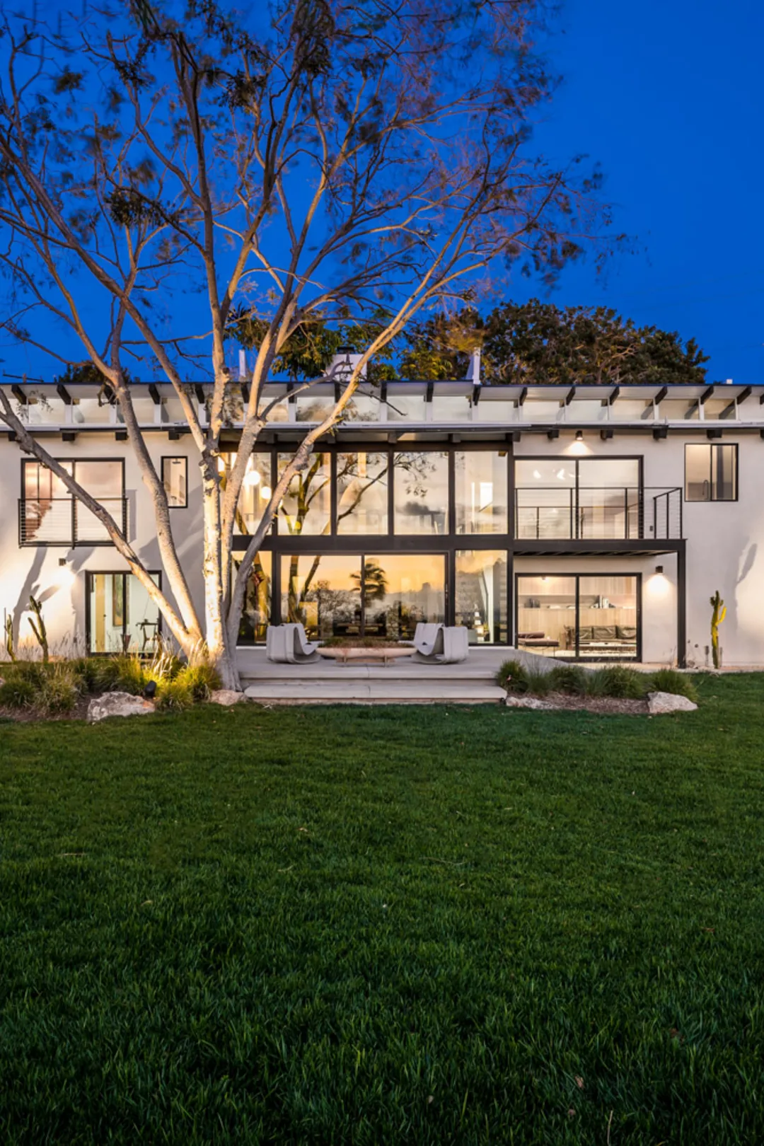 Filaree Heights, Malibu: the house lit from within at dusk, across its lawn.