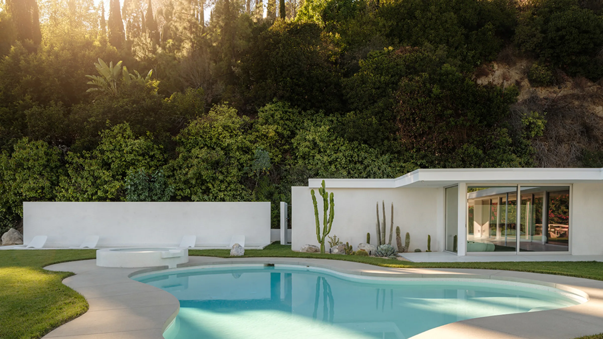 Rising Glen at golden hour: the white single-storey house beyond its freeform pool, sun through the hillside trees.