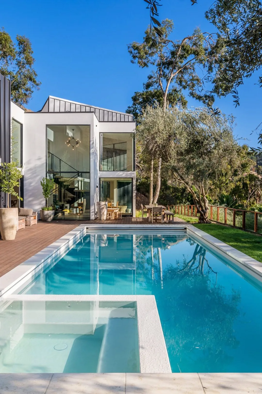Serra Road: the lap pool and wood deck leading to the glass stair tower, olive trees against the hillside.