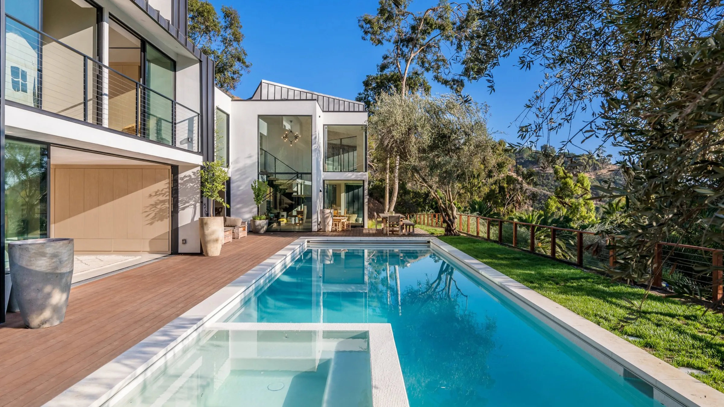 Serra Road: the lap pool and wood deck leading to the glass stair tower, olive trees against the hillside.