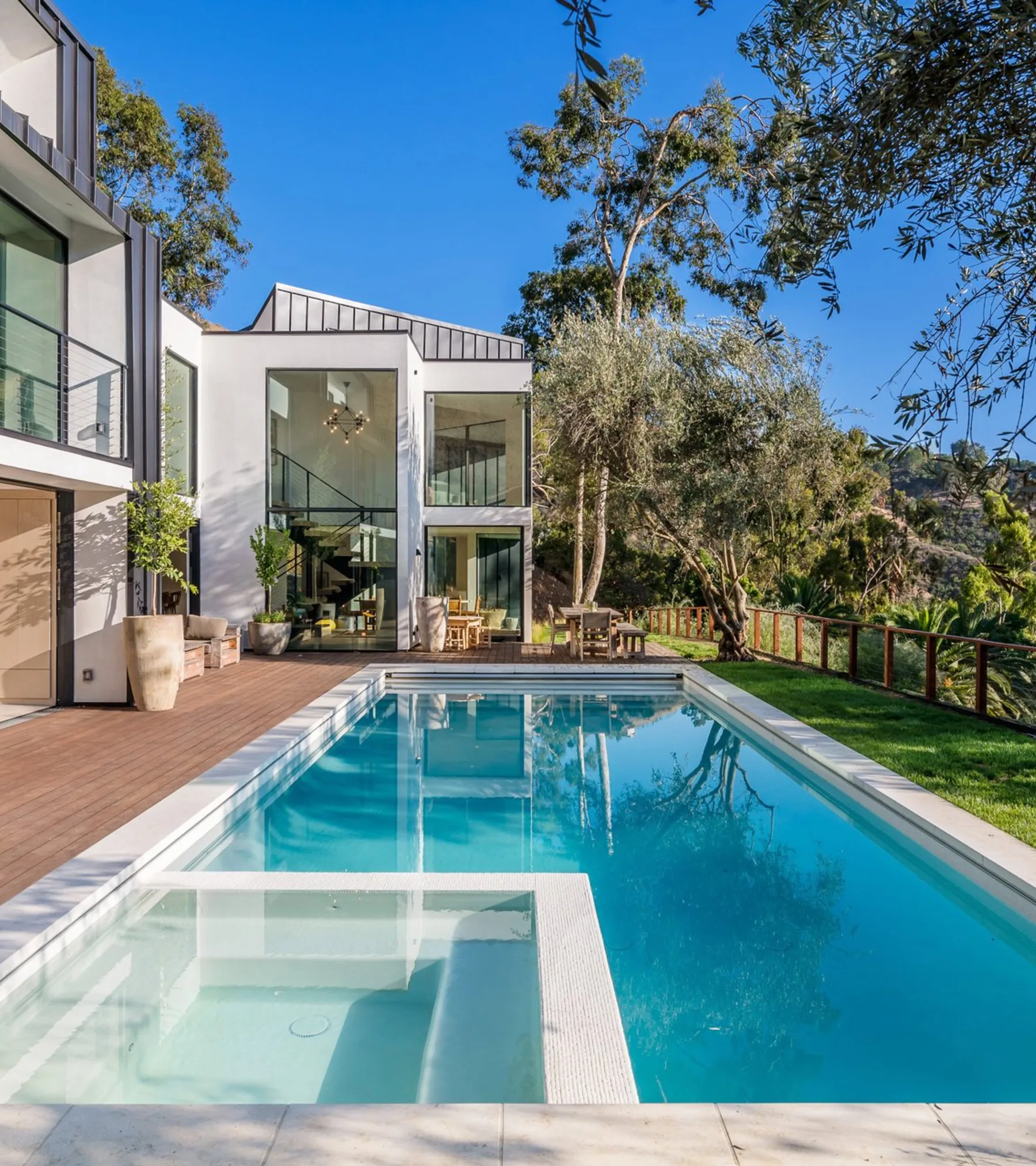 Serra Road: the lap pool and wood deck leading to the glass stair tower, olive trees against the hillside.