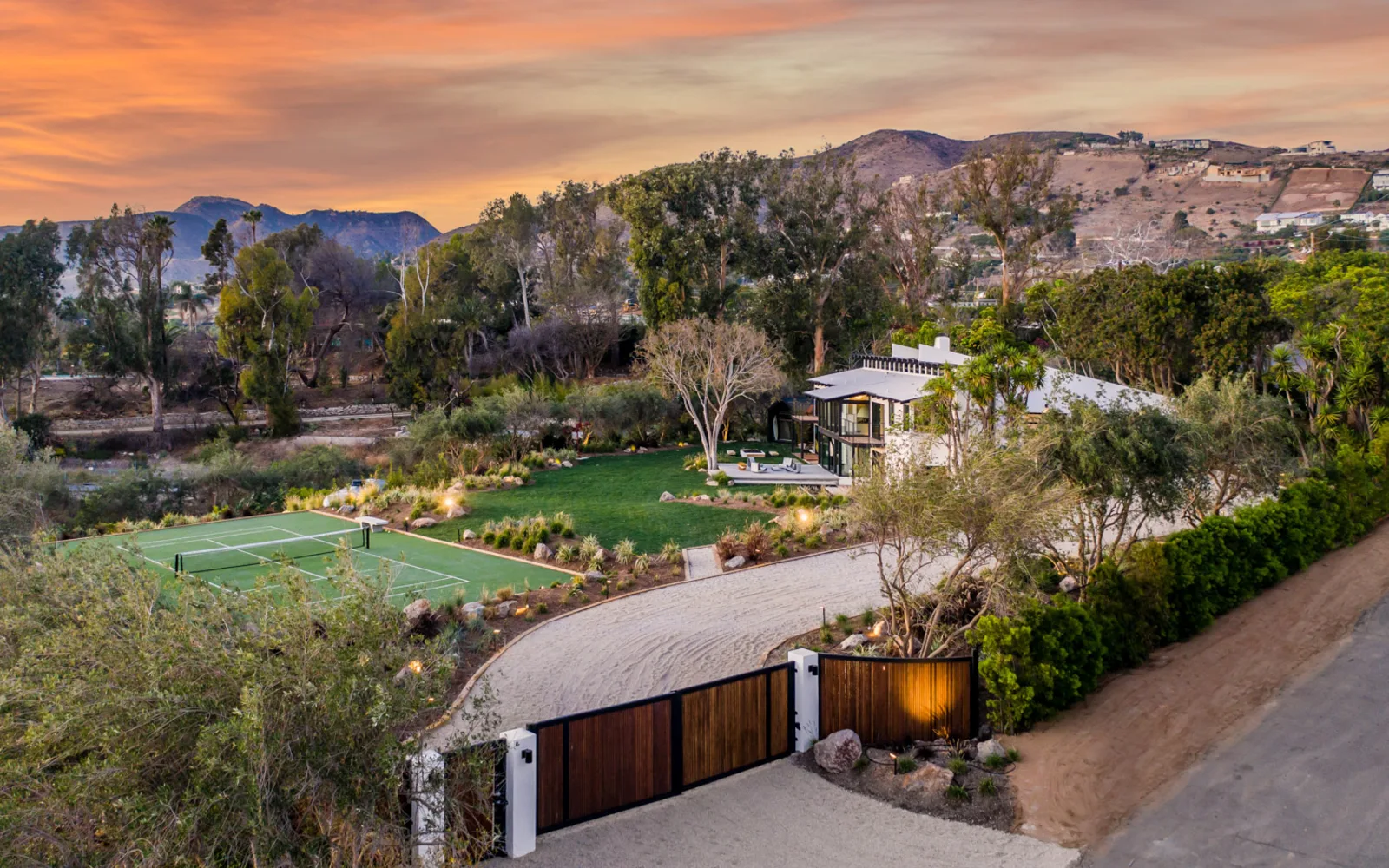 5901 Filaree Heights from the air at dusk: the house, its lawn and court set against the Malibu hills.