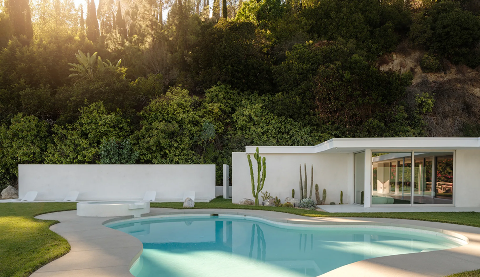 Rising Glen at golden hour: the white single-storey house beyond its freeform pool, sun through the hillside trees.